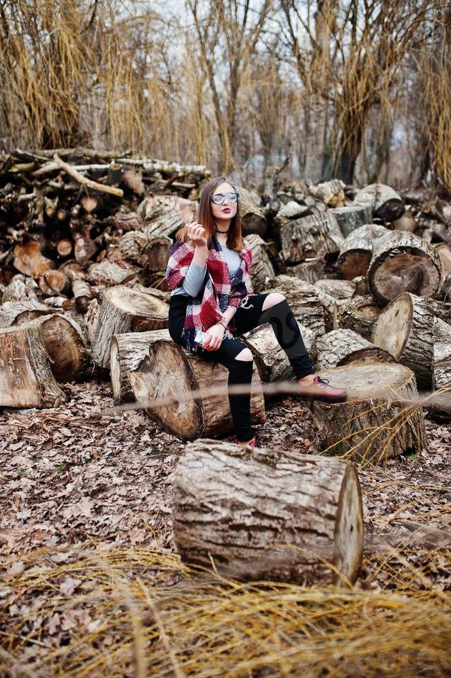 Young girl smoking cigarette outdoors background wooden stumps. Concept of nicotine addiction by teenagers. photo