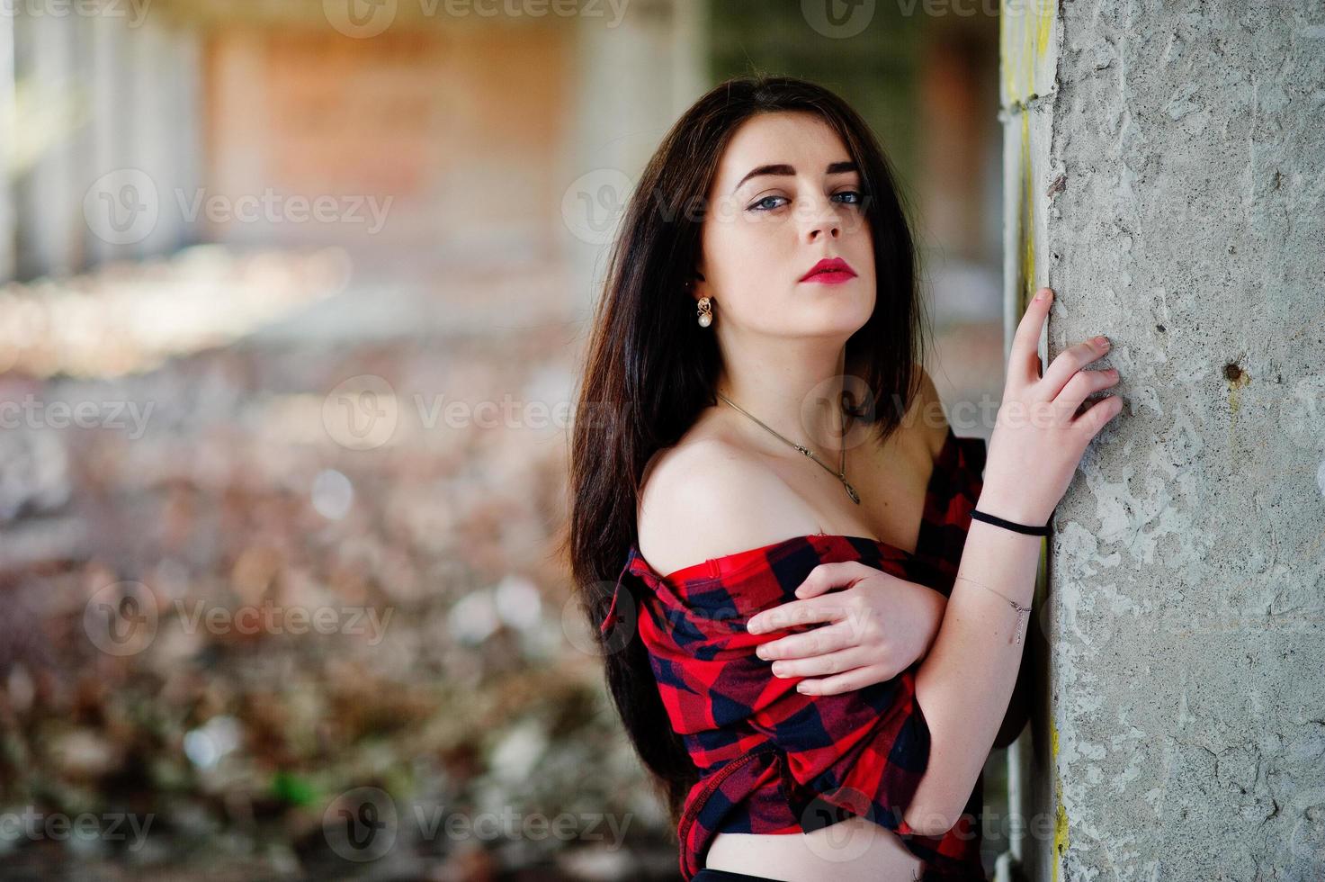 chica de retrato con labios rojos con una camisa a cuadros roja con los hombros desnudos posó un lugar sexy de fondo abandonado. foto