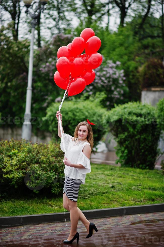 Portrait of a gorgeous beautiful bridesmaid in a pretty dress holding heart-shaped red balloons in the park at bachelorette party. photo