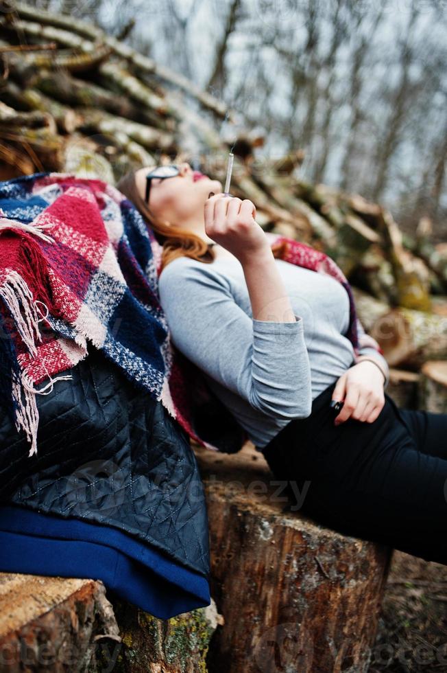 Young girl smoking cigarette outdoors background wooden stumps. Concept of nicotine addiction by teenagers. photo