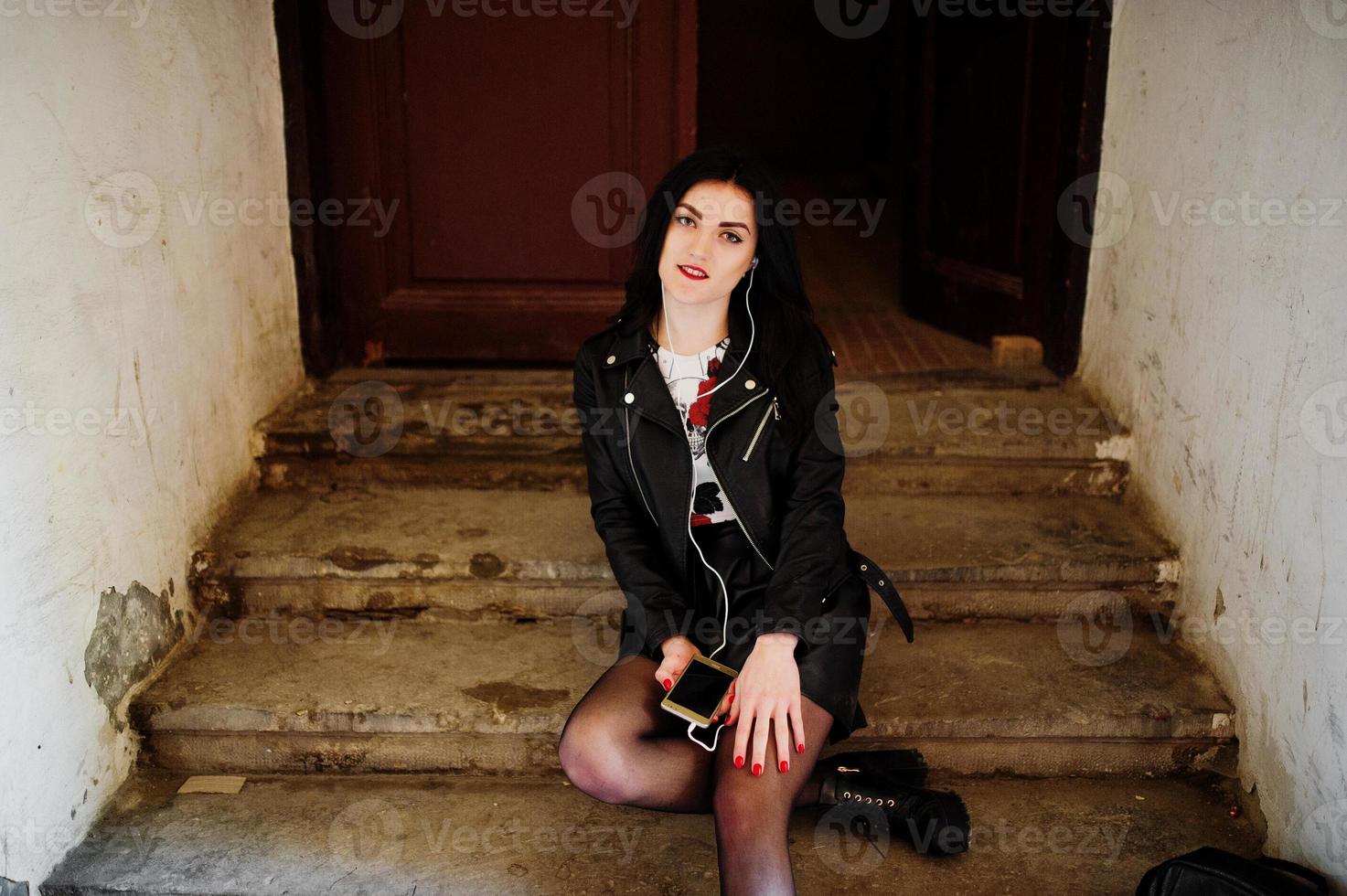 Young goth girl on black leather skirt and jacket posed on stairs of old house. photo