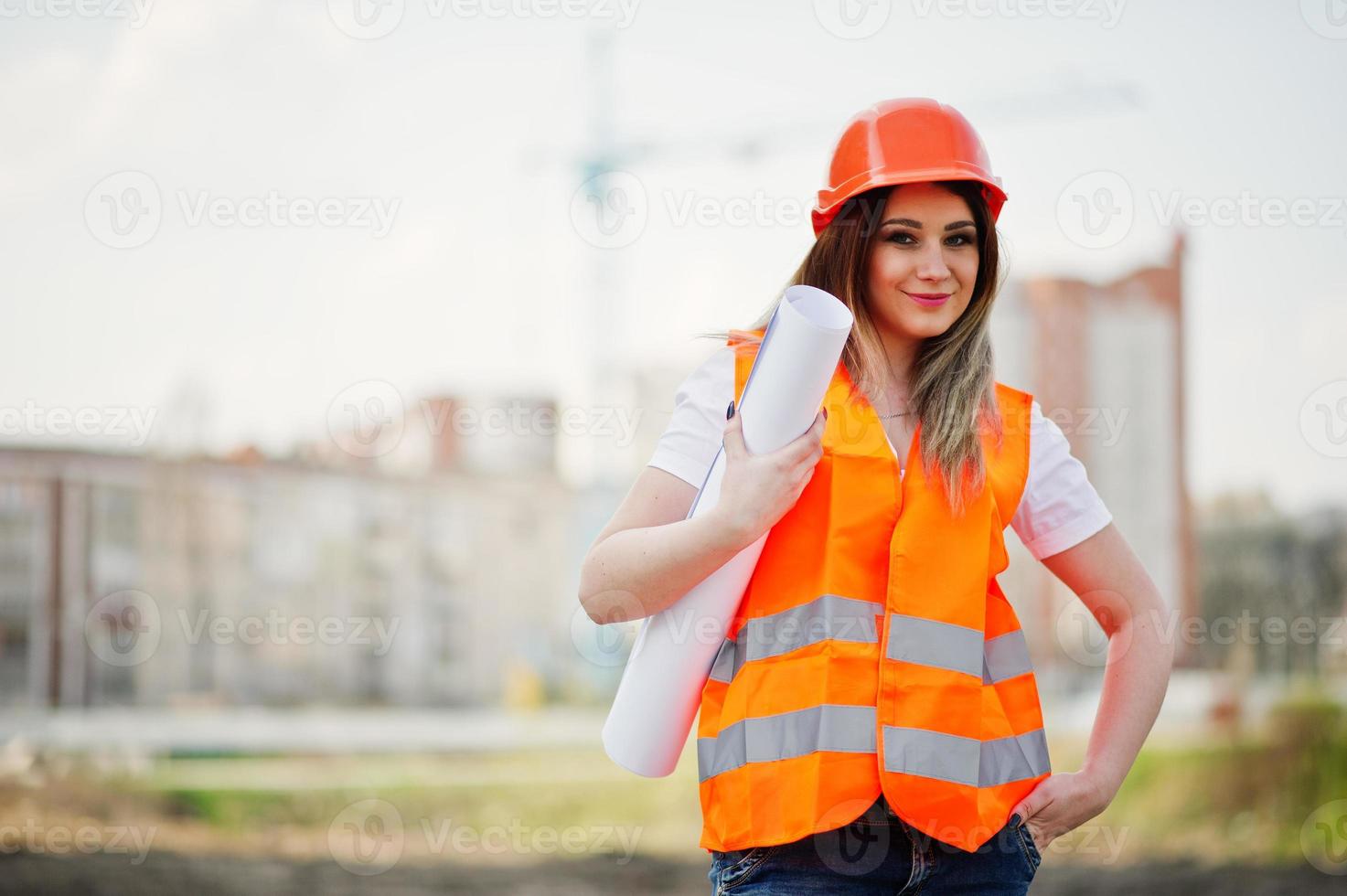 Engineer builder woman in uniform waistcoat and orange protective helmet hold business paper against new buildings with crane. photo