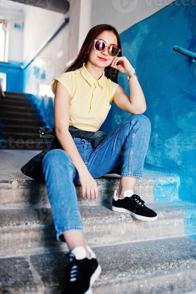 Young teenage girl sitting on stairs of house entrance, wear on yellow t-shirt, jeans and sunglasses. photo