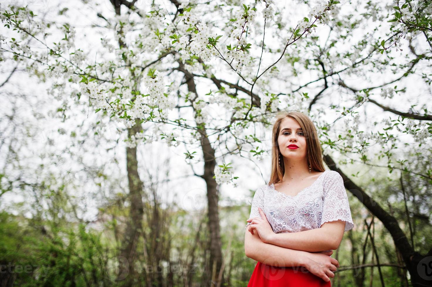 Portrait of beautiful girl with red lips at spring blossom garden, wear on red dress and white blouse. photo