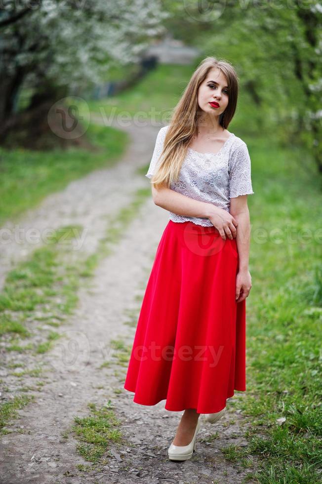 retrato de una hermosa chica con labios rojos en el jardín de flores de primavera, vestido rojo y blusa blanca. foto