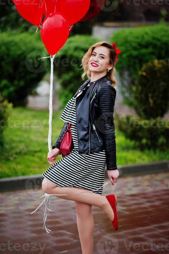 Portrait of a gorgeous beautiful bridesmaid in a pretty dress holding heart-shaped red balloons in the park at bachelorette party. photo