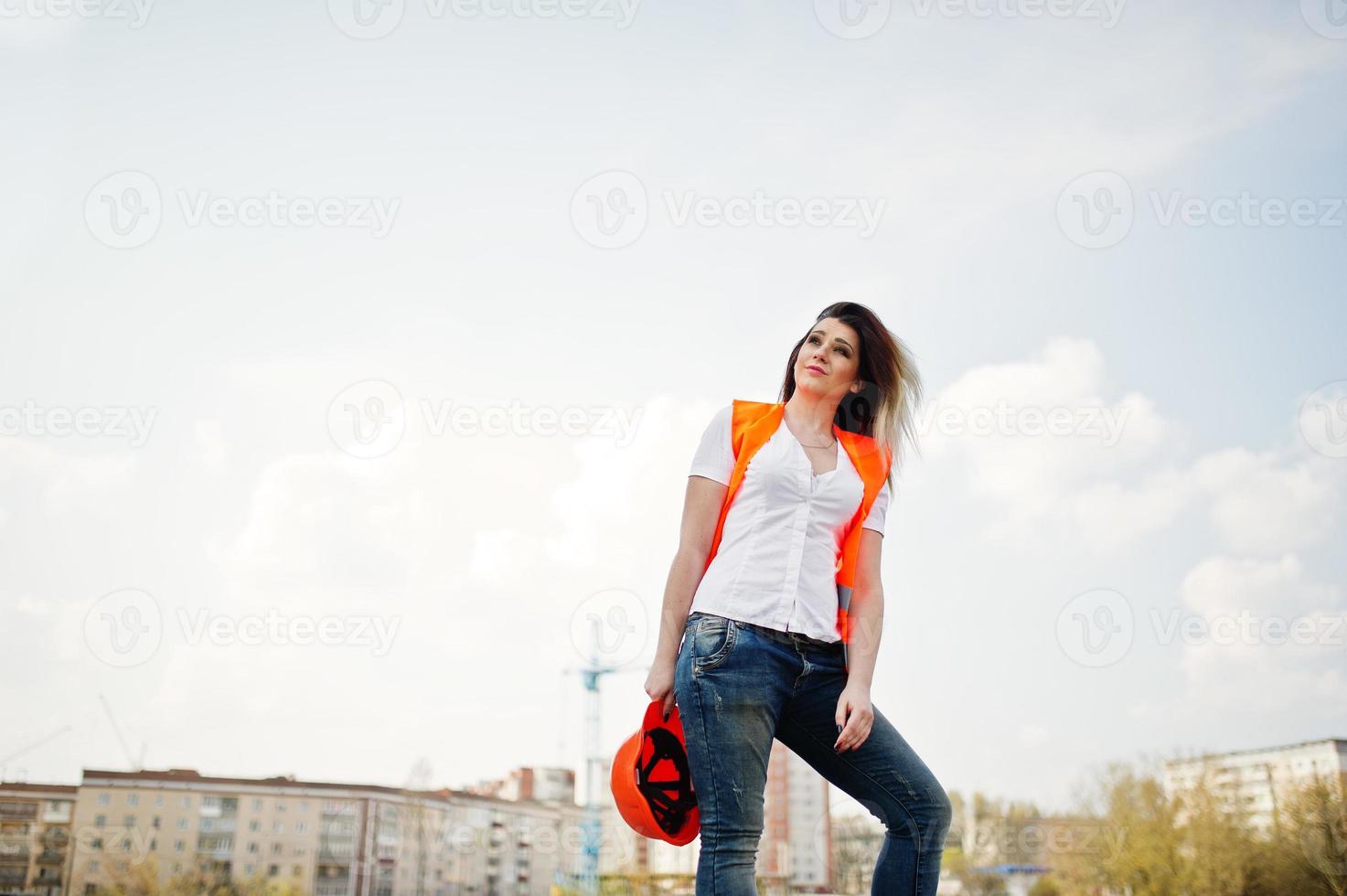 Engineer builder woman in uniform waistcoat and orange protective helmet against new buildings. photo