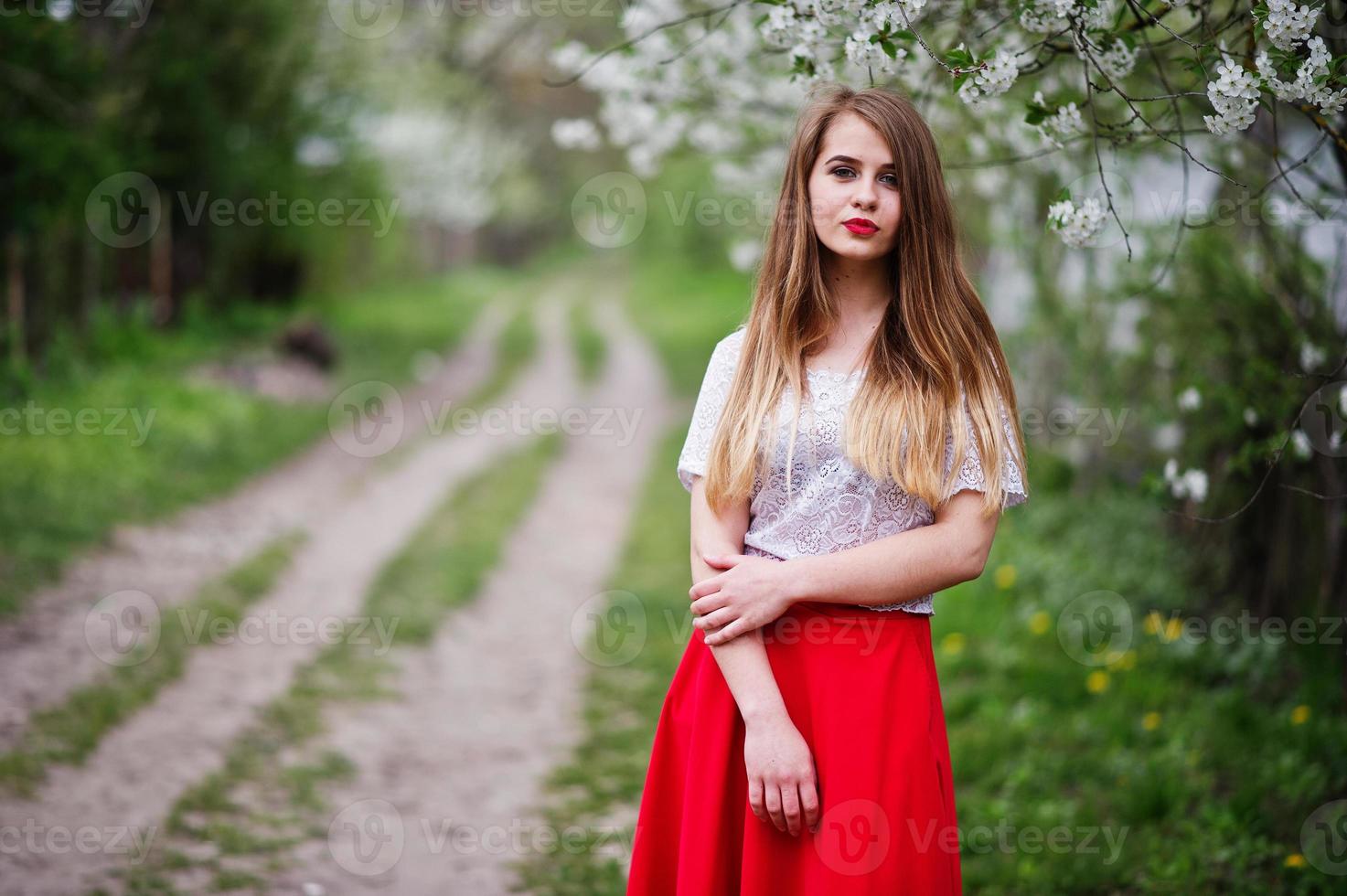 Portrait of beautiful girl with red lips at spring blossom garden, wear on red dress and white blouse. photo