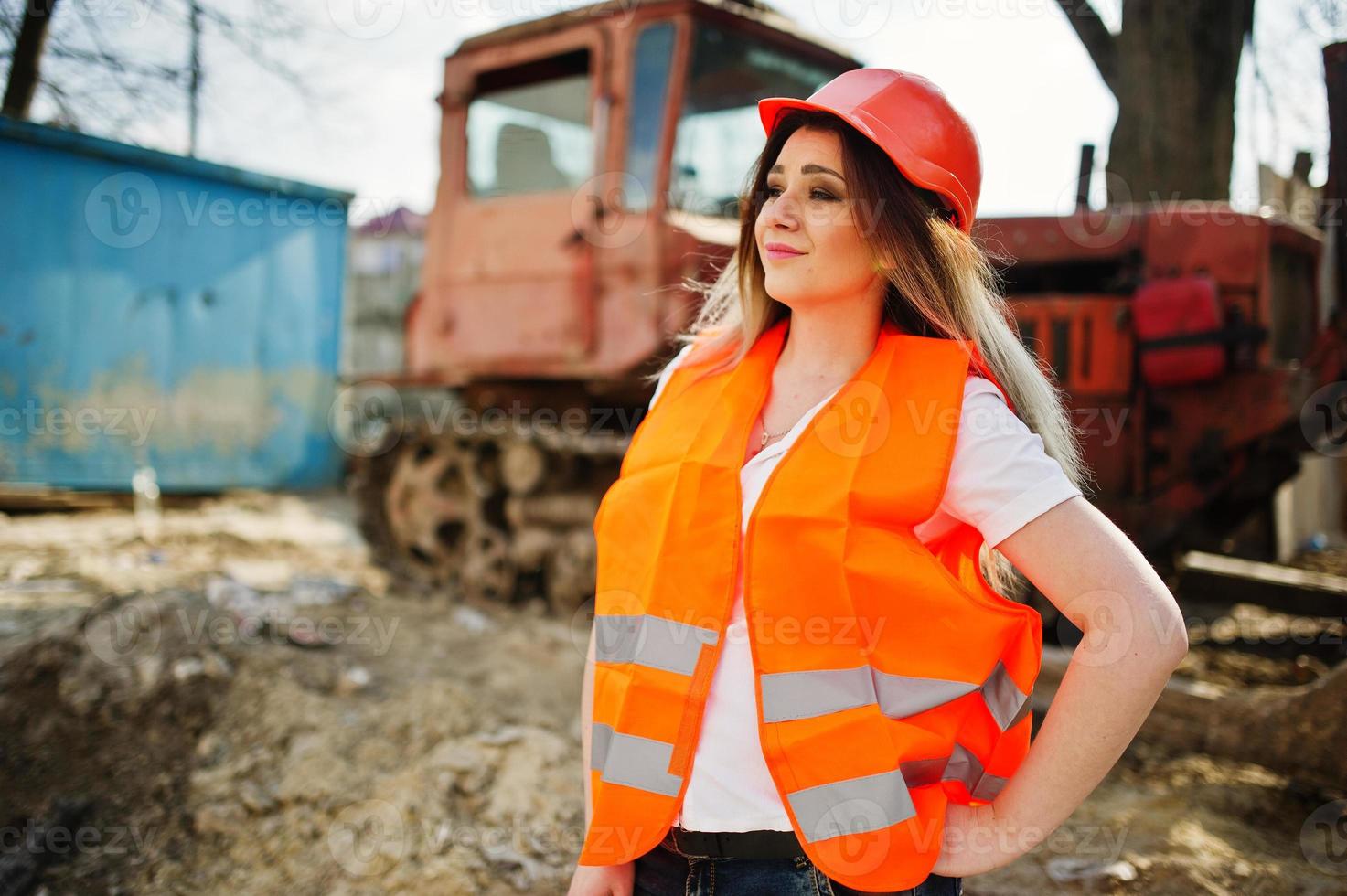 mujer ingeniera constructora con chaleco uniforme y casco protector naranja contra bulldozer. foto