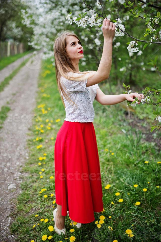 Portrait of beautiful girl with red lips at spring blossom garden, wear on red dress and white blouse. photo