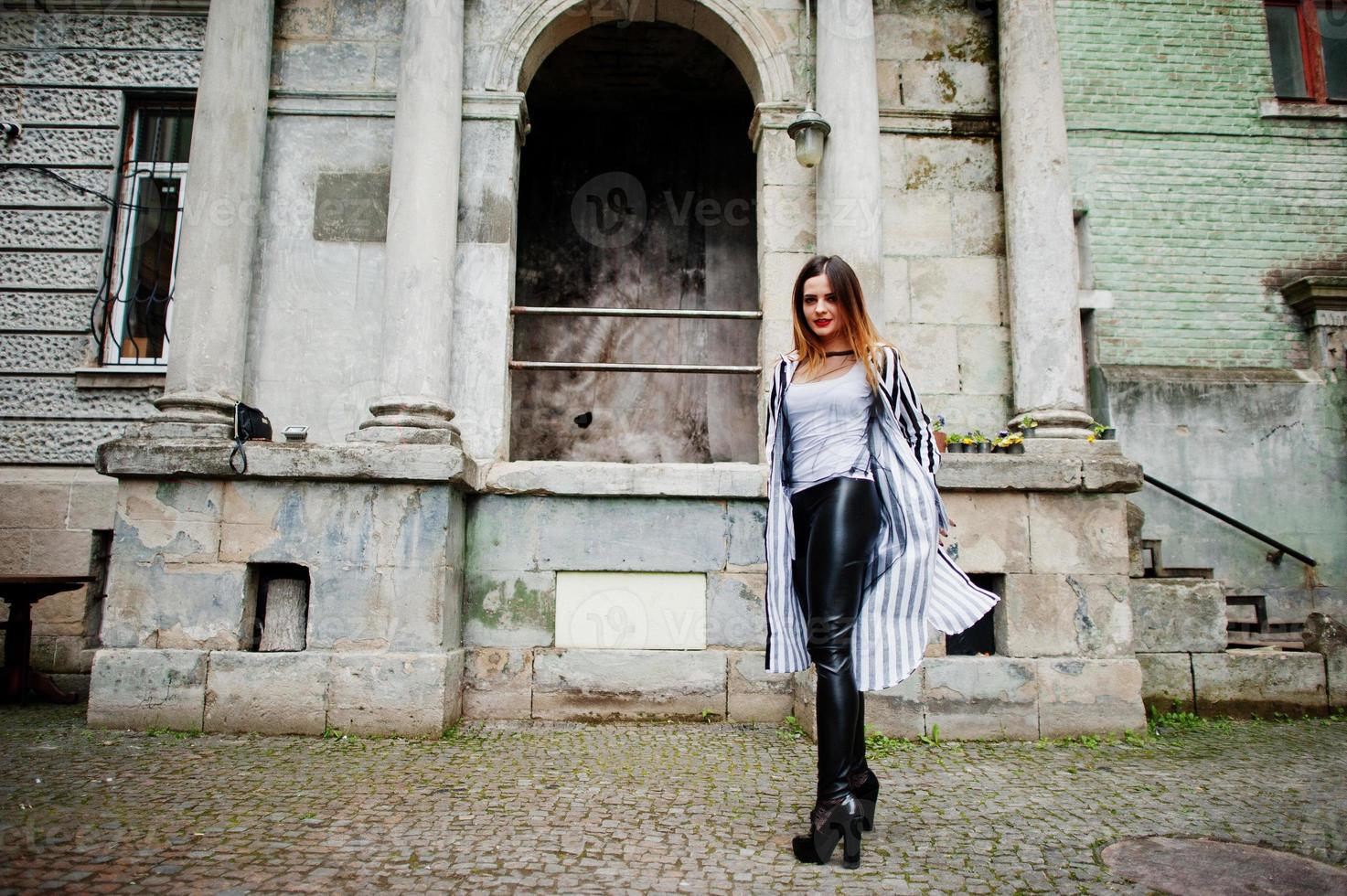 Fashionable woman look with black and white striped suit jacket, leather pants,  posing at old street. Concept of fashion girl. photo