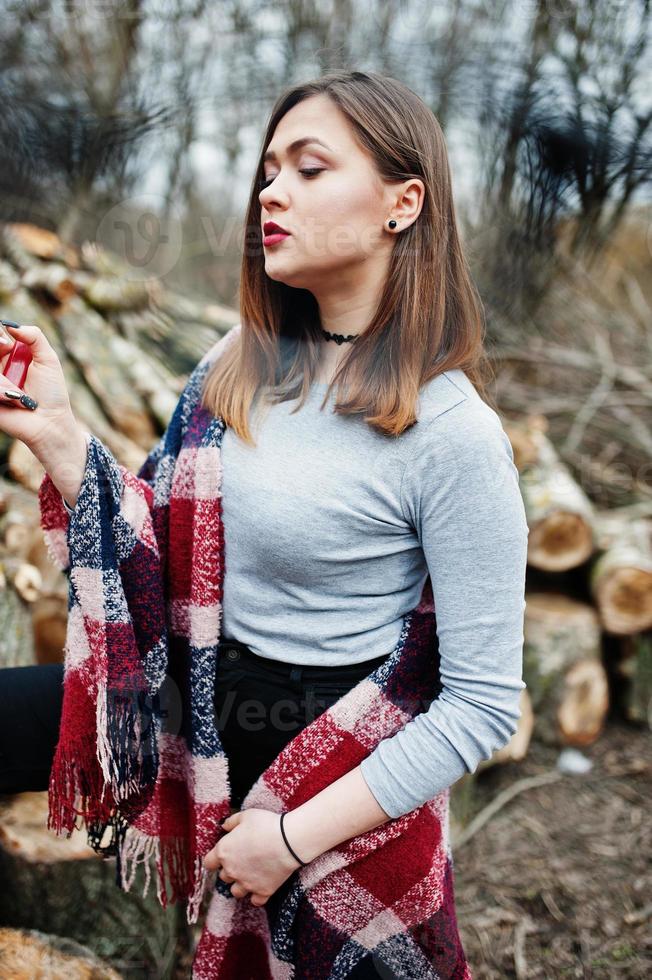 Young girl smoking cigarette outdoors background wooden stumps. Concept of nicotine addiction by teenagers. photo