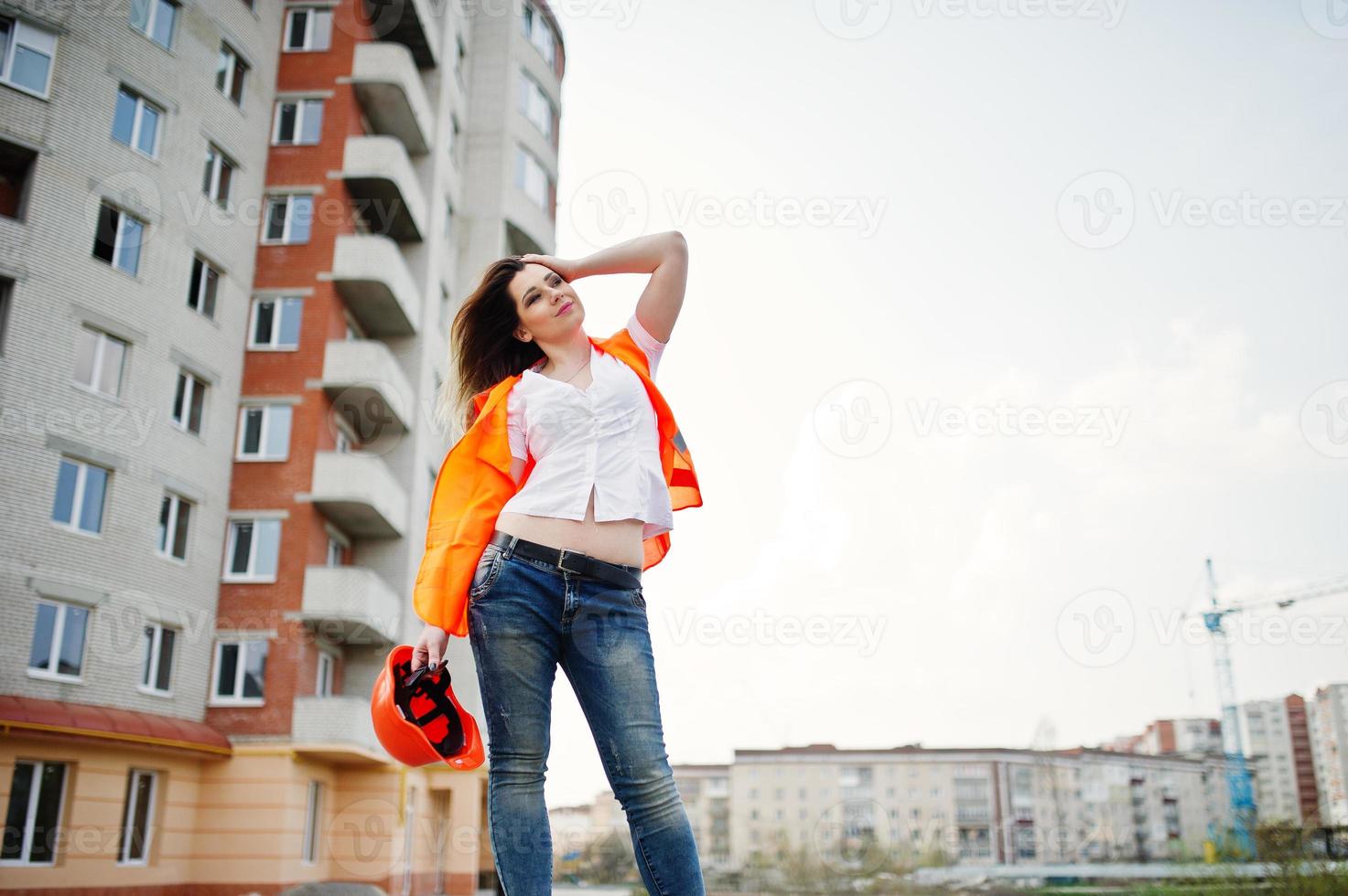 mujer ingeniera constructora con chaleco uniforme y casco protector naranja contra nuevos edificios. foto