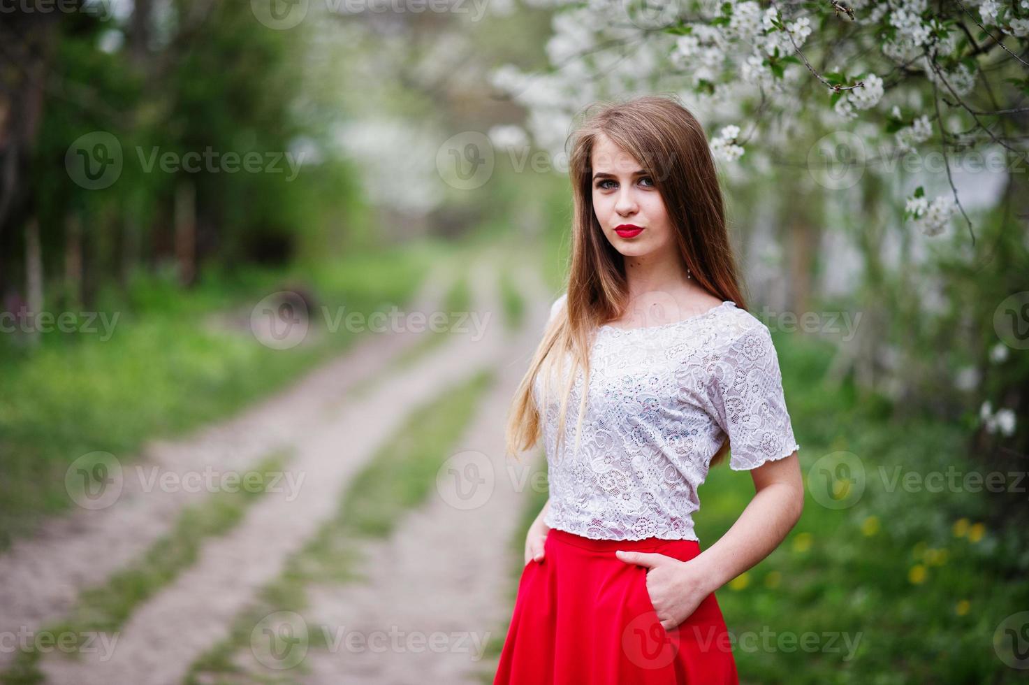 retrato de una hermosa chica con labios rojos en el jardín de flores de primavera, vestido rojo y blusa blanca. foto