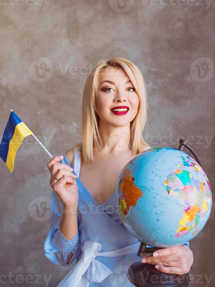 beautiful attractive cheerful blonde Slavic woman holding globe and ukrainian flag. photo