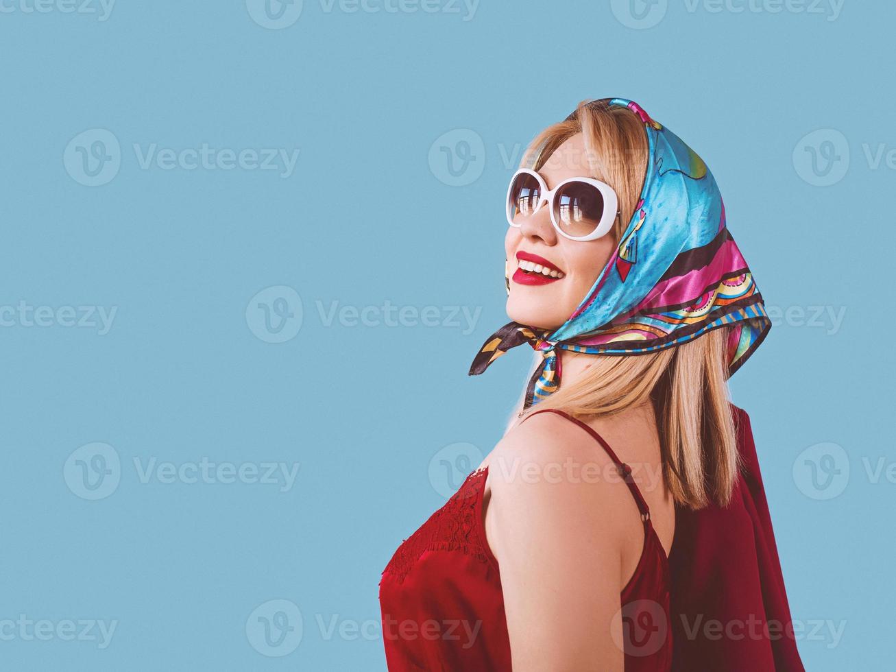 stylish smiling cheerful fancy blonde woman with make up in neckerchief and sunglasses on blue background photo