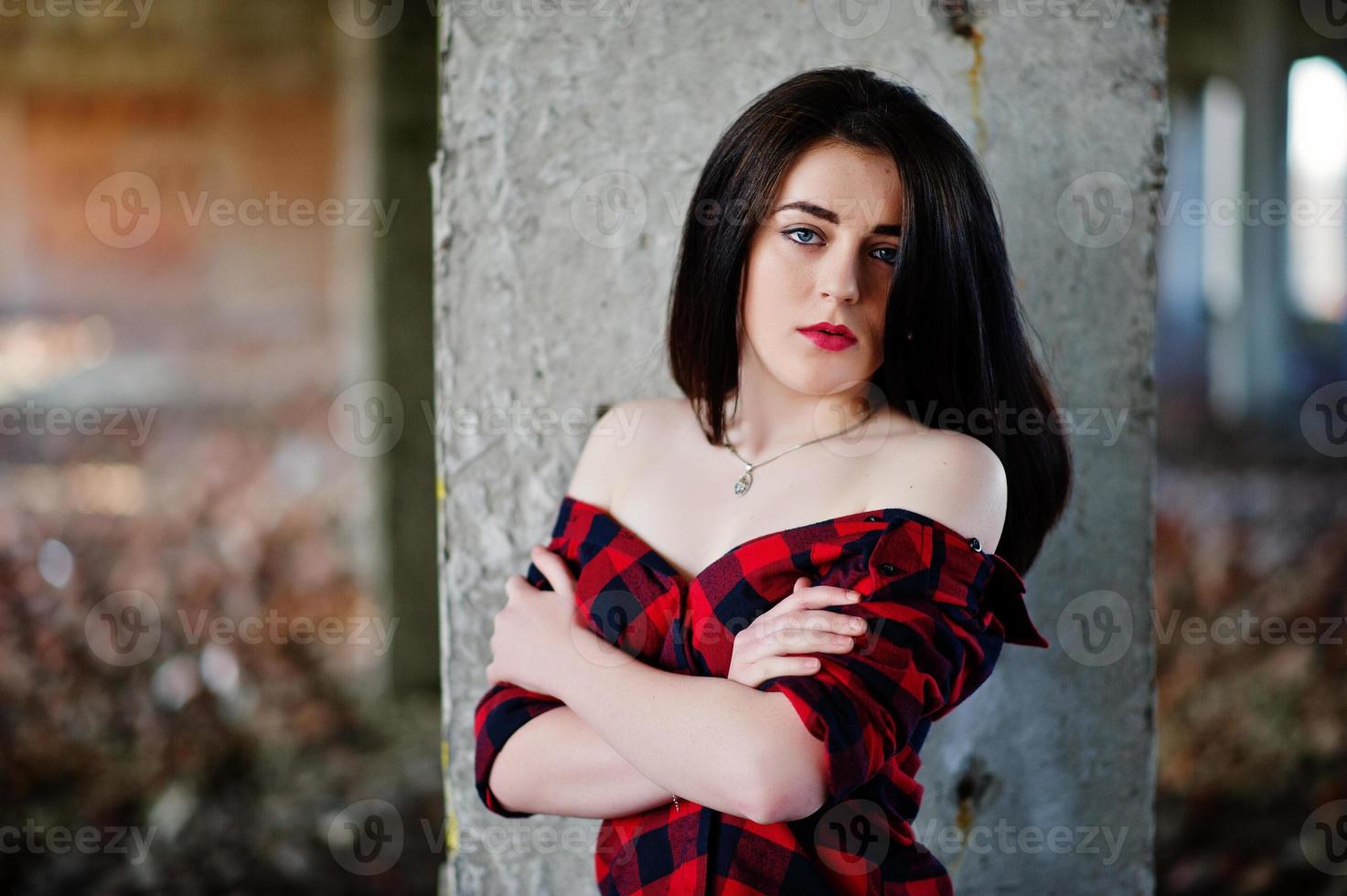 Portrait girl with red lips wearing a red checkered shirt with bare shoulders posed sexy background abadoned place. photo