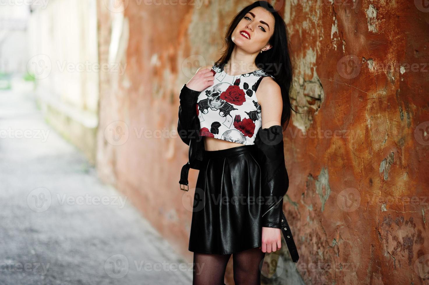 Young goth girl on black leather skirt and jacket against grunge wall. photo