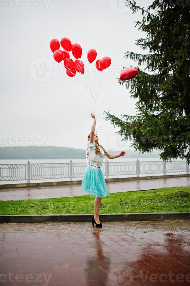 Portrait of a gorgeous beautiful bridesmaid in a pretty dress holding heart-shaped red balloons in the park at bachelorette party. photo