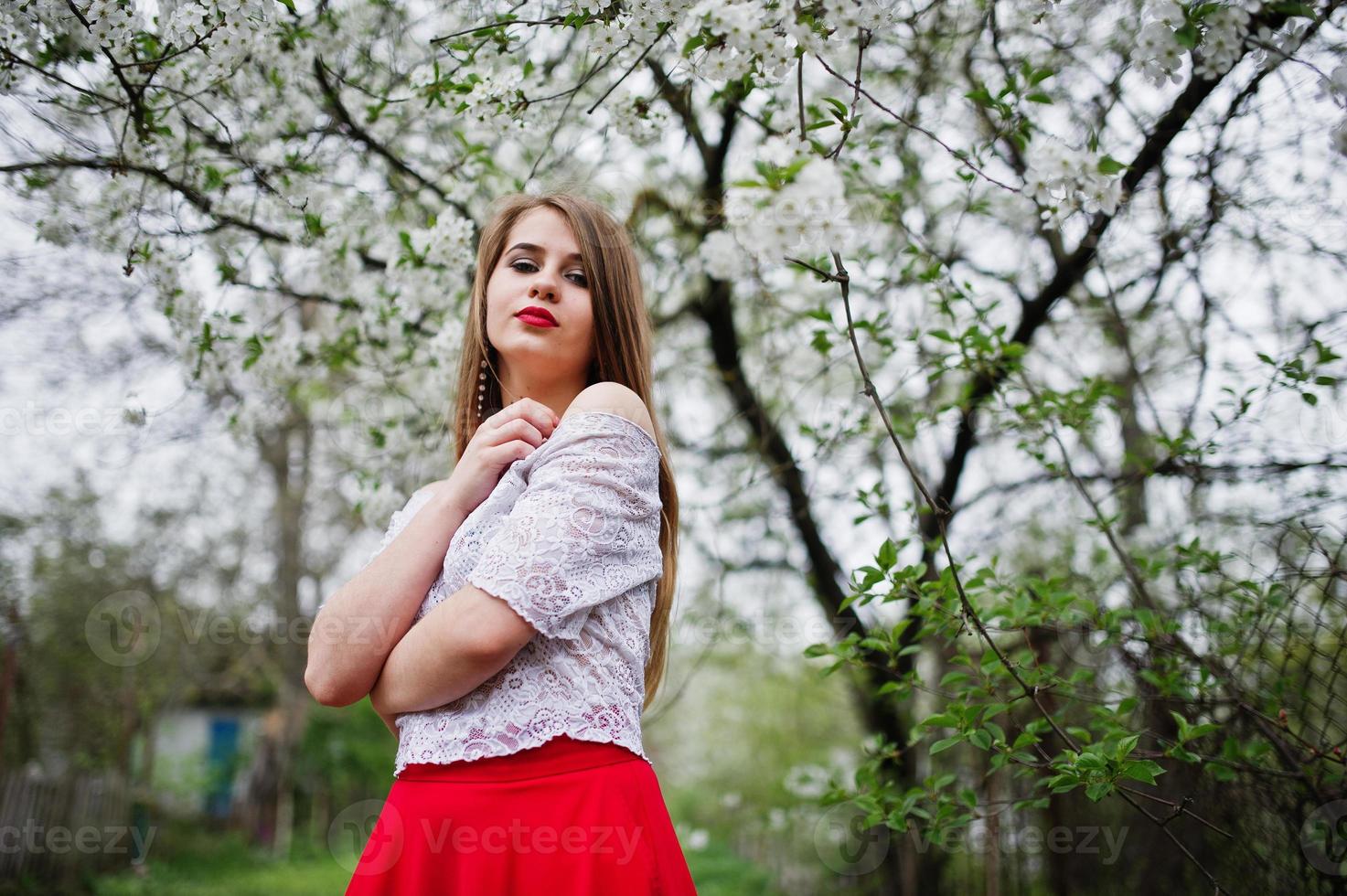 retrato de una hermosa chica con labios rojos en el jardín de flores de primavera, vestido rojo y blusa blanca. foto