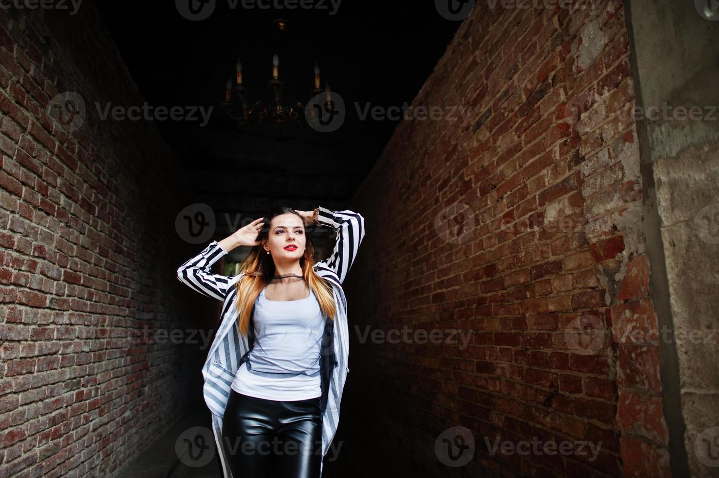 Fashionable woman look with black and white striped suit jacket, leather pants, posing at old street red brick tunnel. Concept of fashion girl. photo