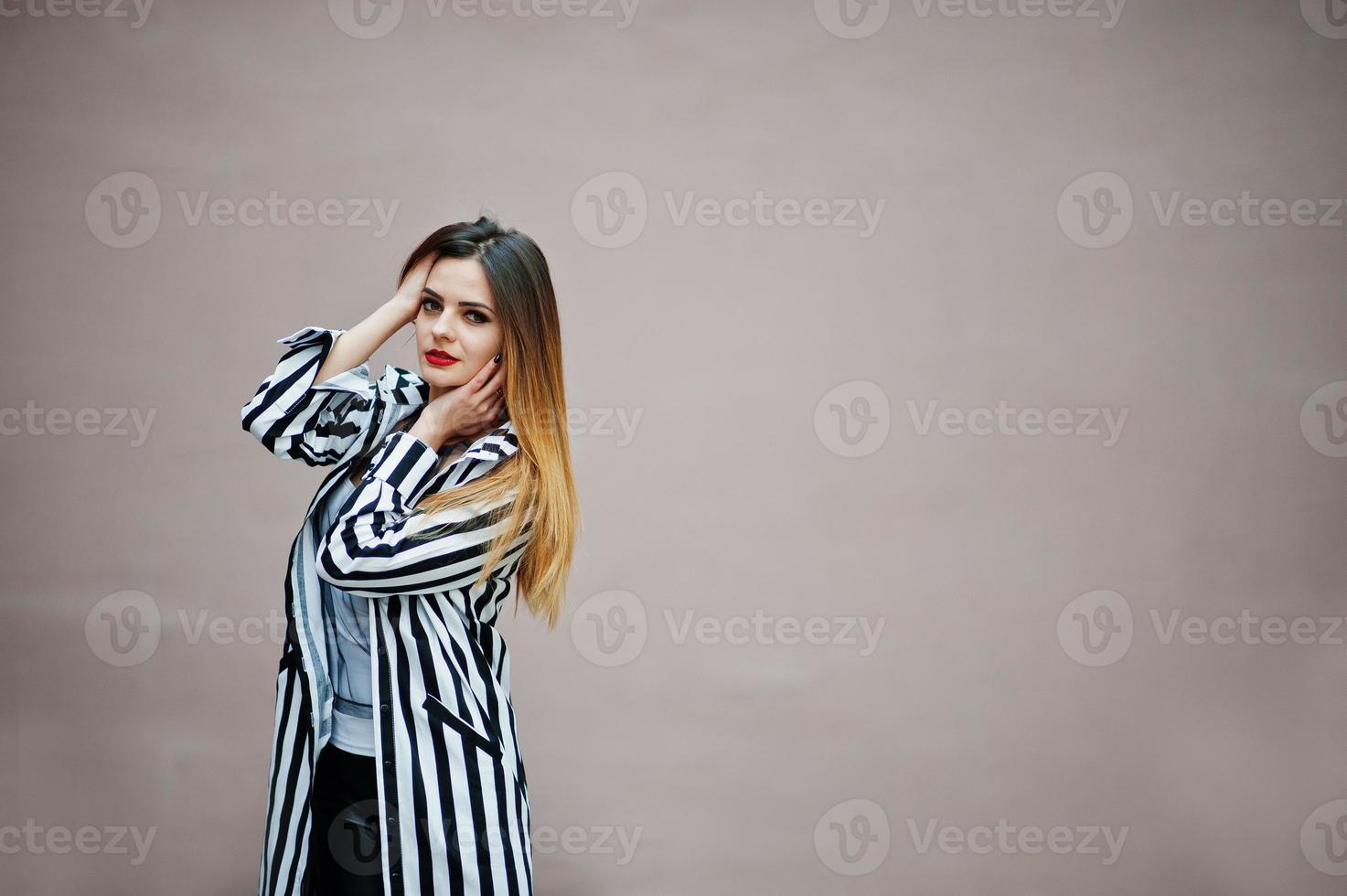Fashionable woman look with black and white striped suit jacket, leather pants posing against wall. Concept of fashion girl. photo