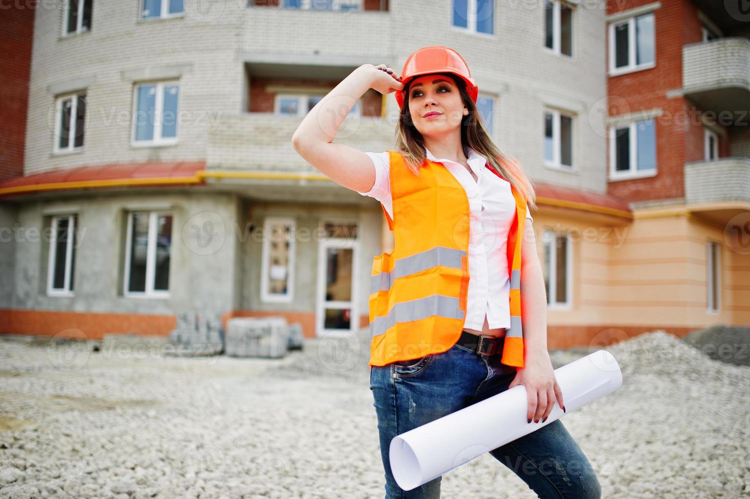 Engineer builder woman in uniform waistcoat and orange protective helmet hold business paper against new building. Property living block theme. photo