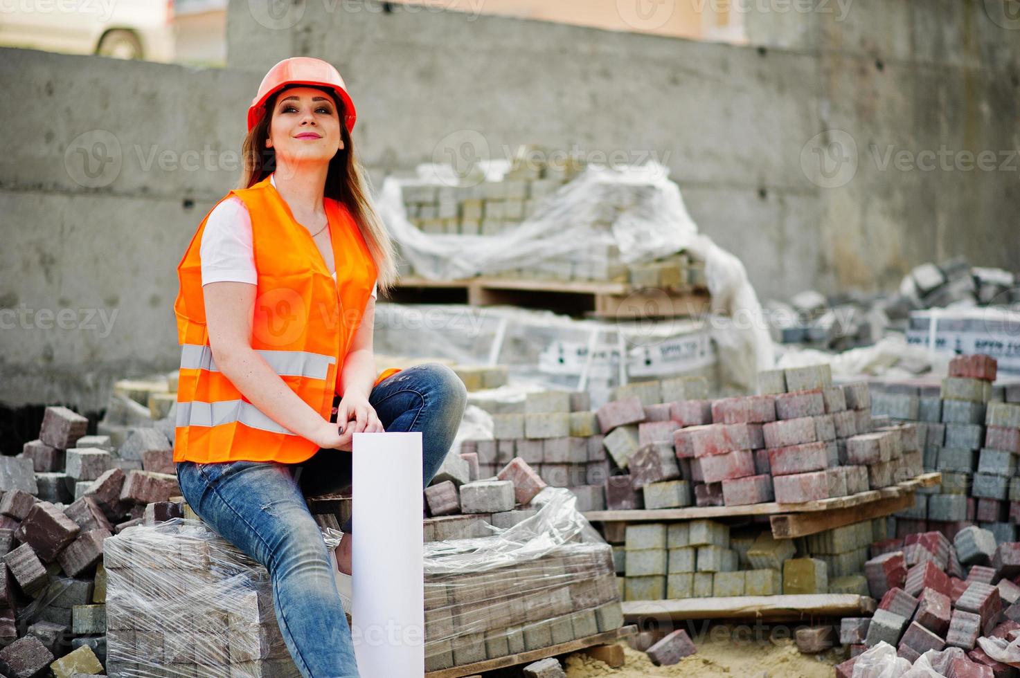 Engineer builder woman in uniform waistcoat and orange protective helmet hold business layout plan paper sitting on pavement. photo