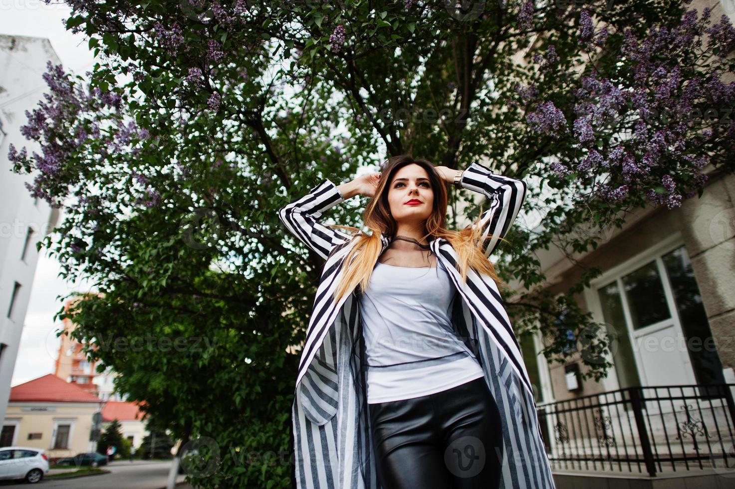 Fashionable woman look with black and white striped suit jacket, posing against lilac tree. Concept of fashion girl. photo