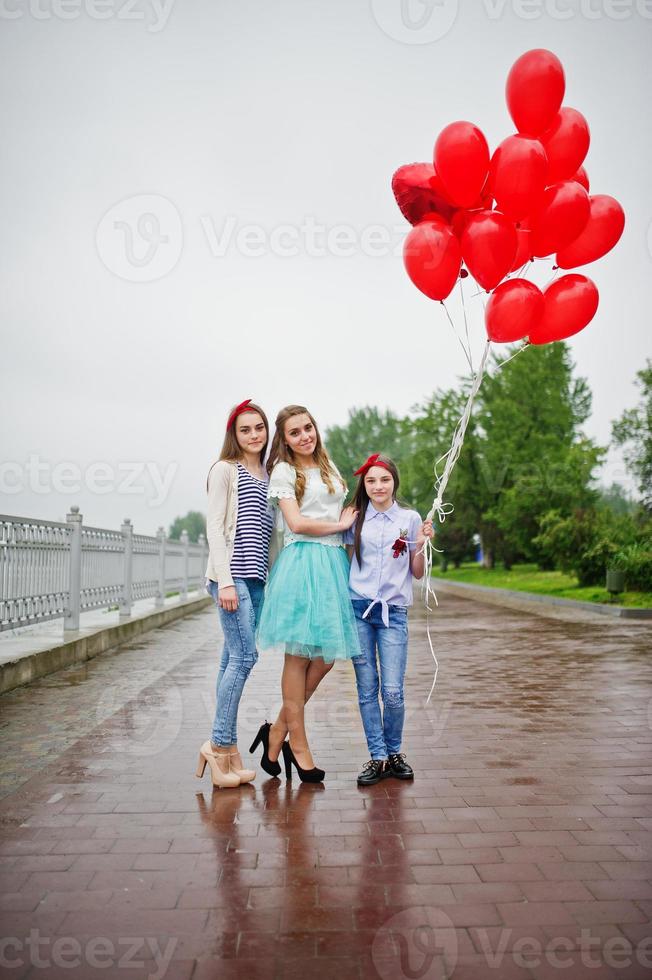 Attractive bride posing with her three lovely bridesmaids with red heart-shaped balloons on the pavement with lake on the background. Bachelorette party. photo