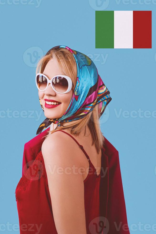 Elegante mujer rubia de fantasía alegre sonriente con maquillaje en pañuelo y gafas de sol sobre fondo azul. foto