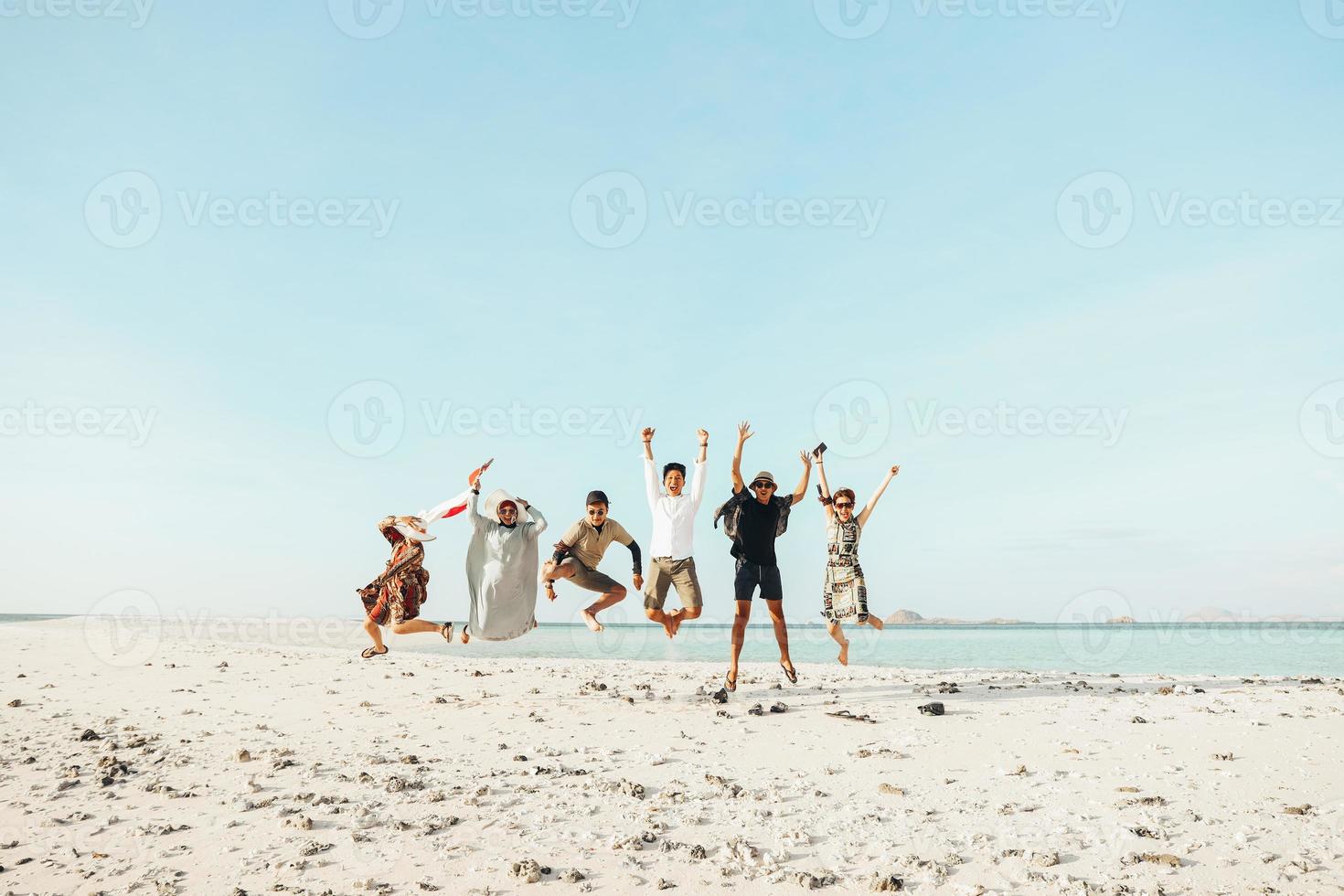 Group of excited Asian people enjoying vacation with jumping together on the beach photo