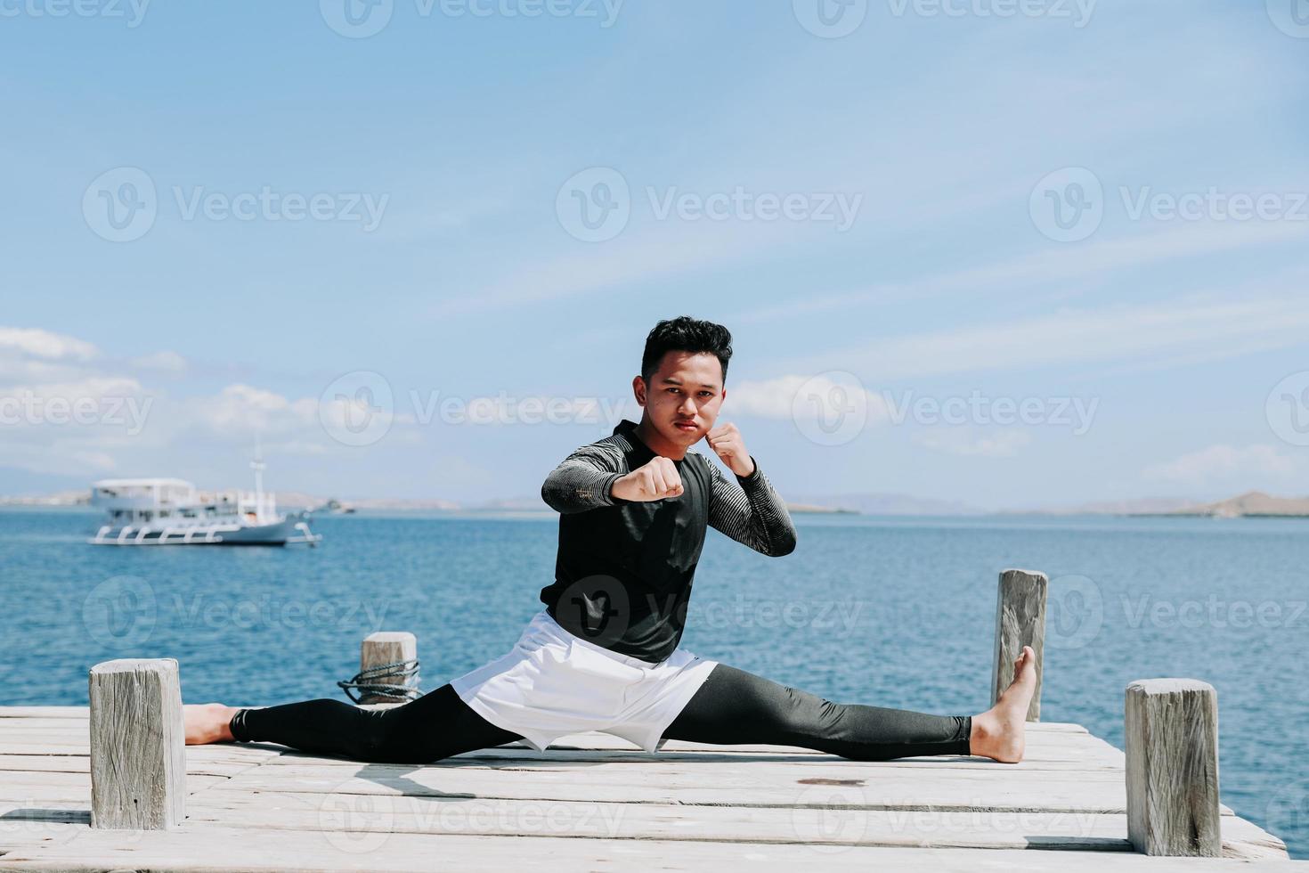 Taekwondo guy sitting with split legs style with sea background photo