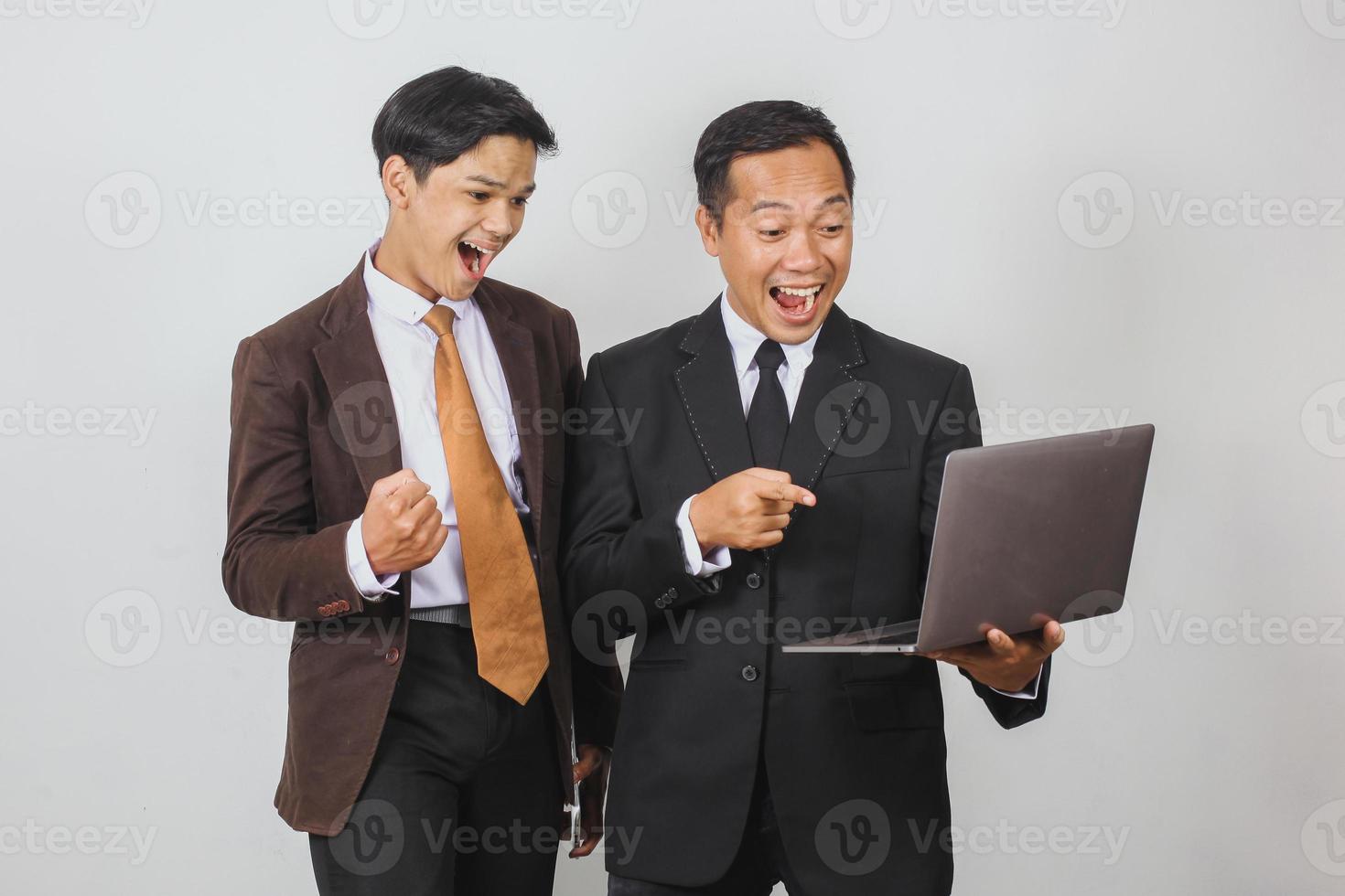 Happy two Asian businessman in suit using a laptop with shocked expression and winning gesture photo