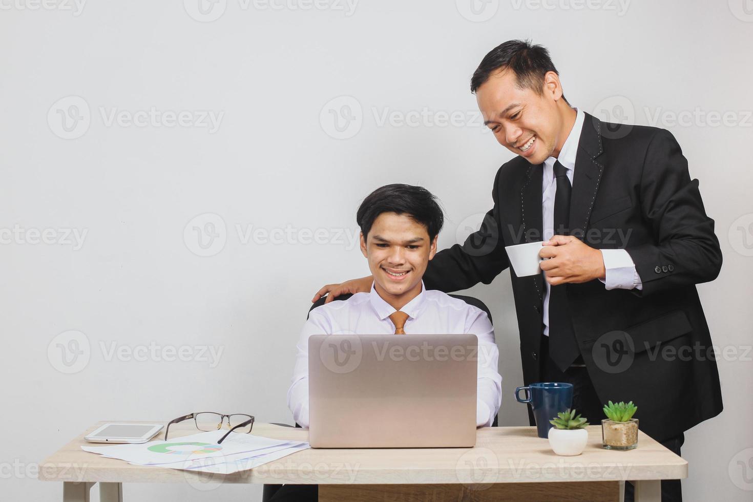 amable jefe asiático sosteniendo una taza y sus empleados hombro que trabajan en el escritorio de la oficina foto