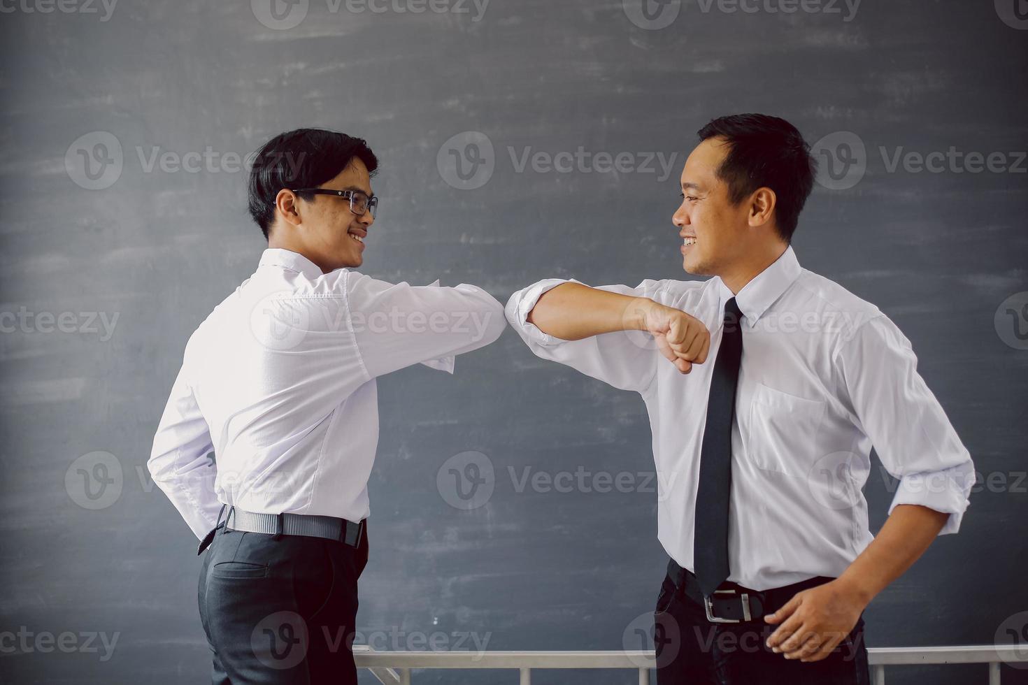 dos hombres de negocios asiáticos con camisas blancas golpeando el codo para evitar el virus de la corona foto