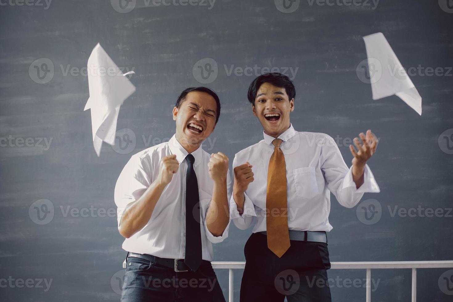 Two happy Asian businessmen celebrating their success and achievements with sheets of paper flying around them photo