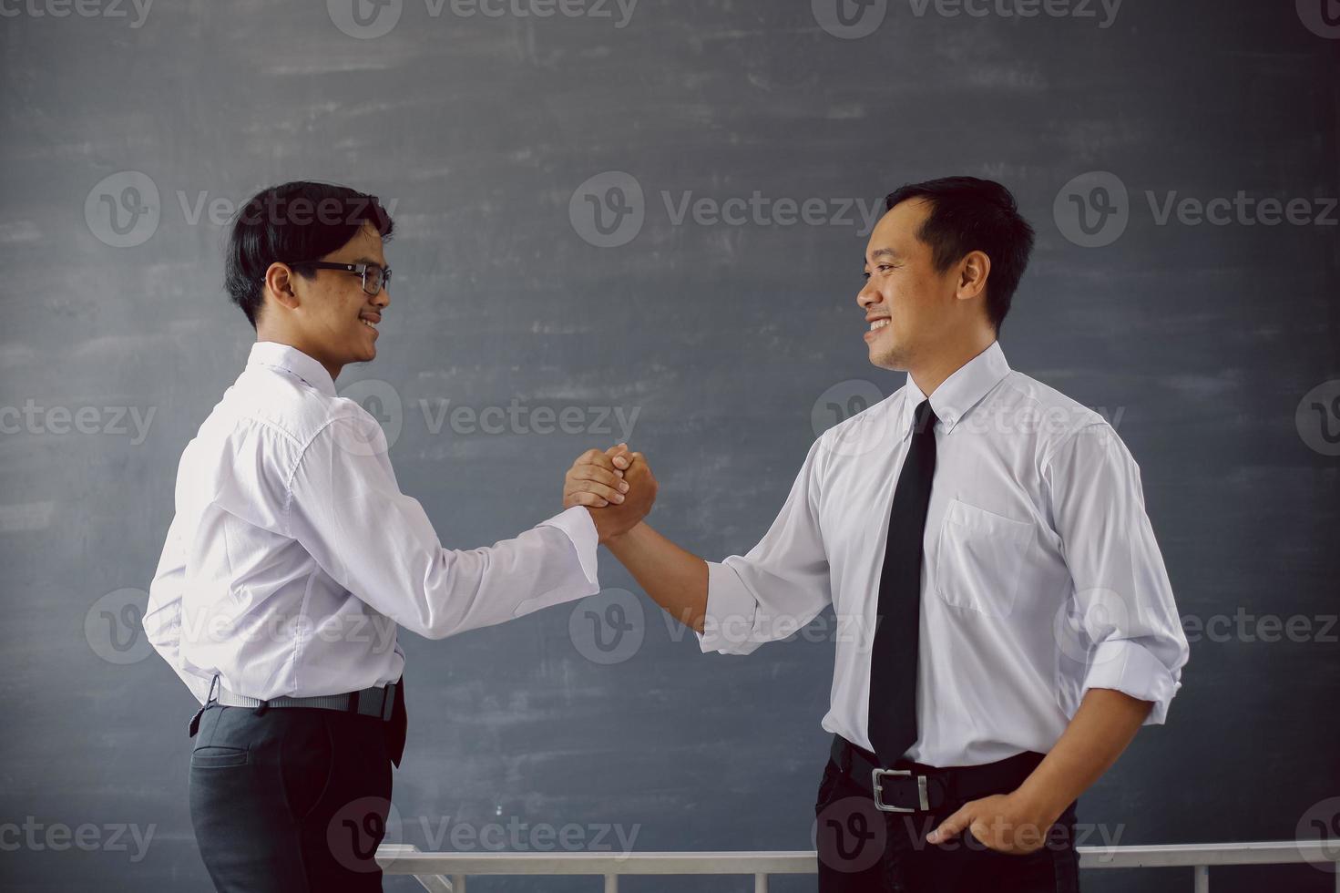 Successful two Asian businessman in shirt and tie smiling while doing doing team handshake photo