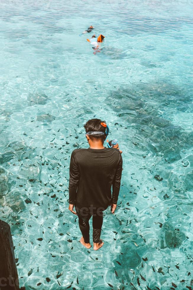 un hombre en traje de neopreno saltando con estilo de pie en el mar transparente con muchos peces marinos foto
