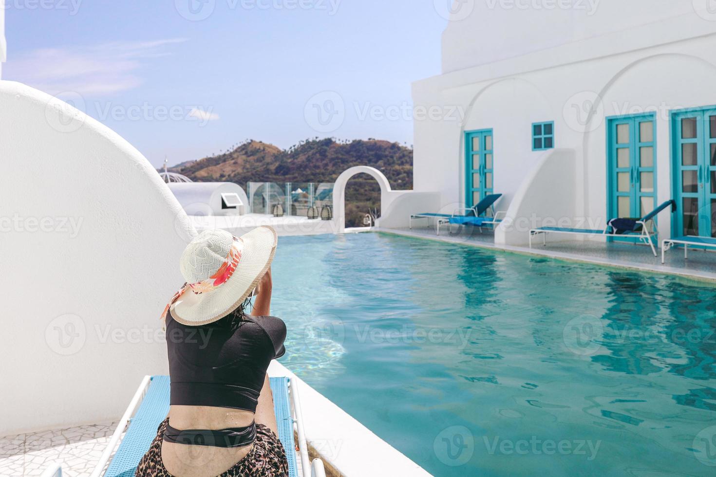 mujer con sombrero de verano sentada en una silla relajante mientras toma el sol junto a la piscina foto