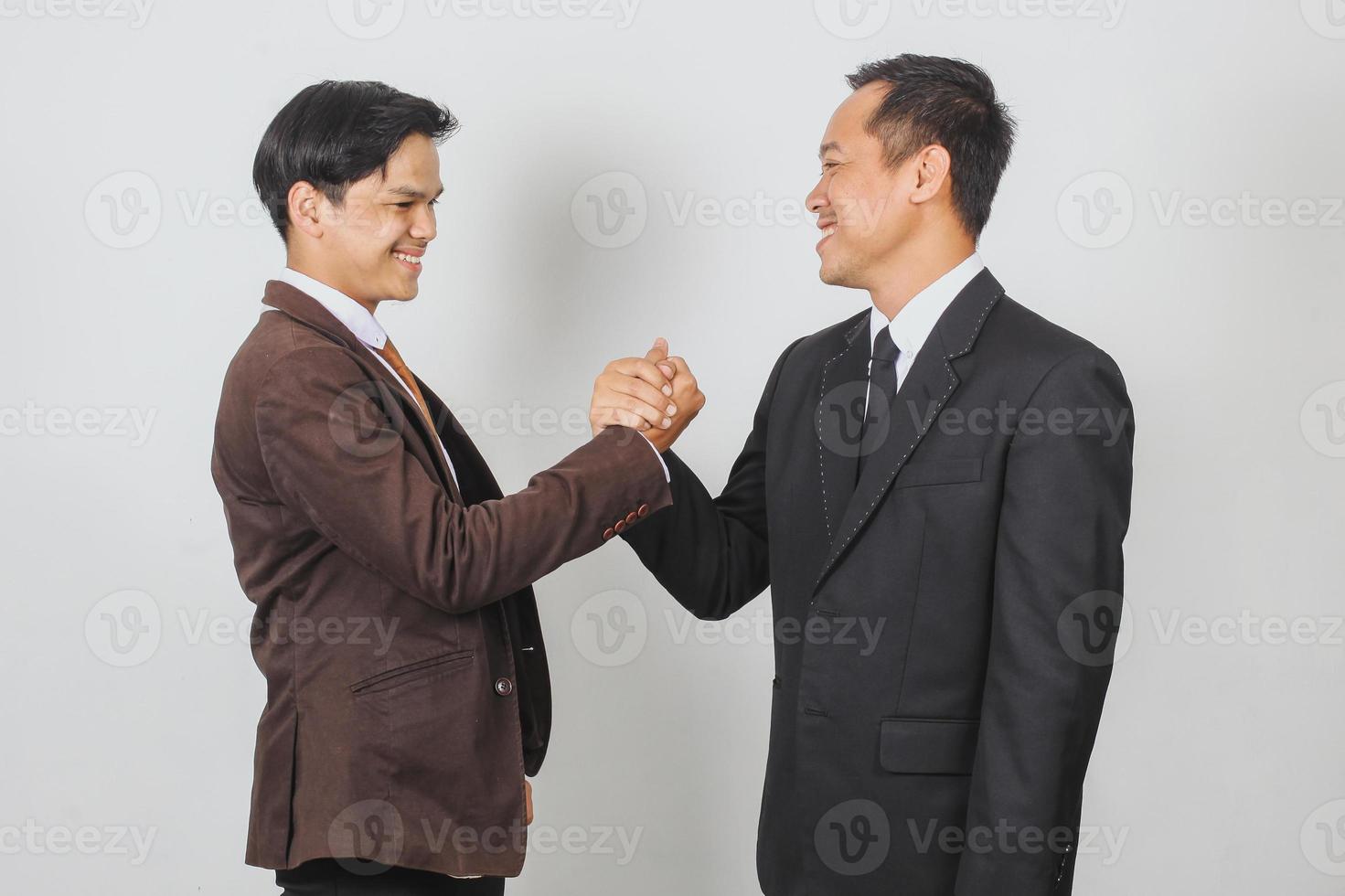 Two Asian businessman in suit and tie looking each other doing team handshake for their success photo