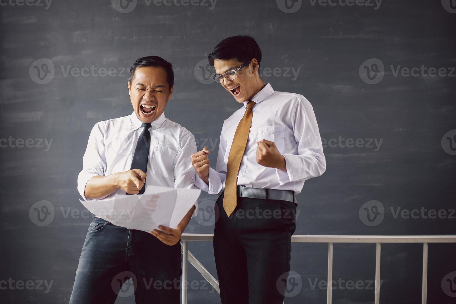 Happy two Asian businessman shocked and surprised looking to paper of report with winning gesture photo