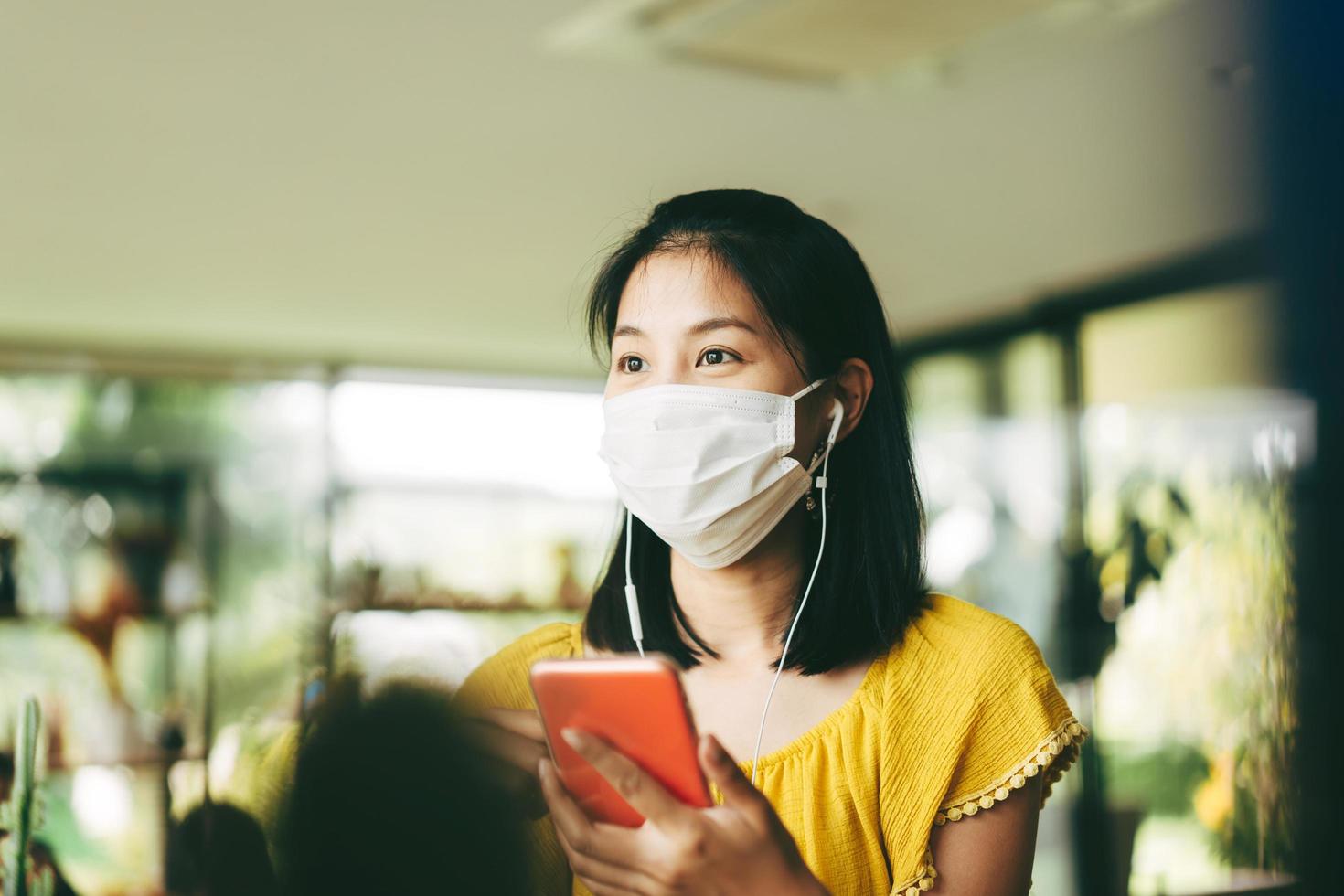 mujer asiática adulta usa máscara para proteger la corona del virus usando el teléfono móvil para la música de la aplicación foto