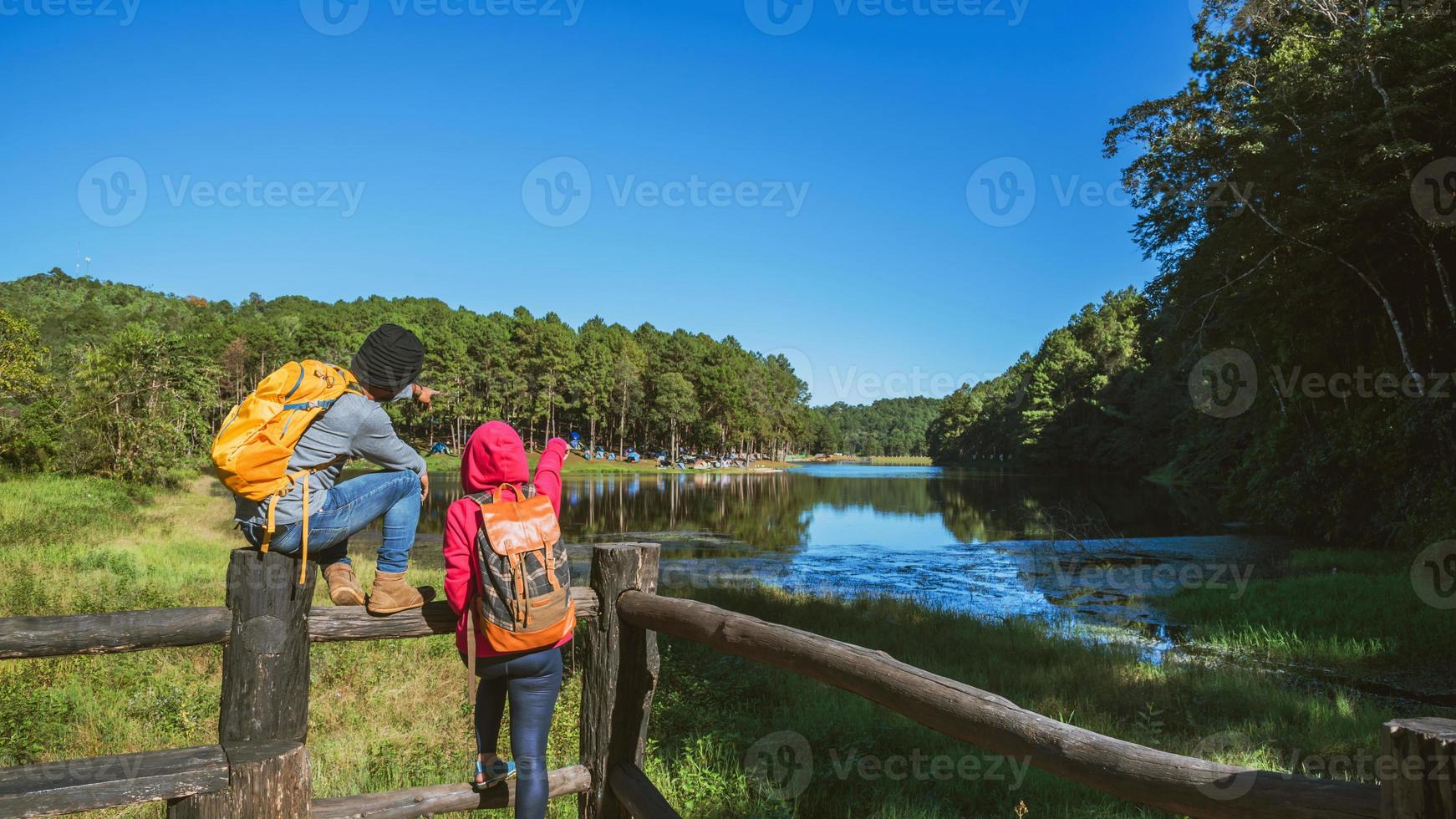 travelers with backpack standing Enjoy the sunrise on the foggy lake surface, Young men and Asian girlfriends travel nature on mountain Pang Ung park in Thailand. photo