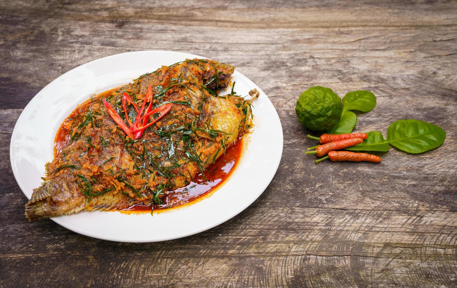 Fried Nile tilapia fish with red curry paste on white plate wooden background, Thai food is spicy mixed with sweet flavor with aromatic spices, Red curry paste is popular to cook in Thailand photo