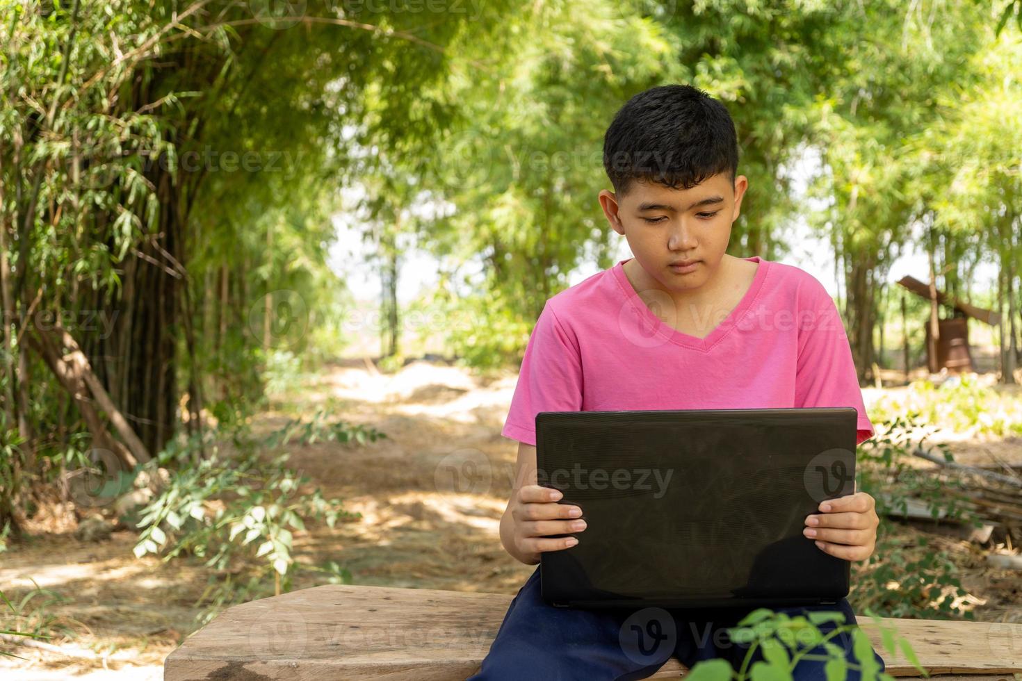 Boy sitting in a chair studying online with laptop computer at home in the countryside photo