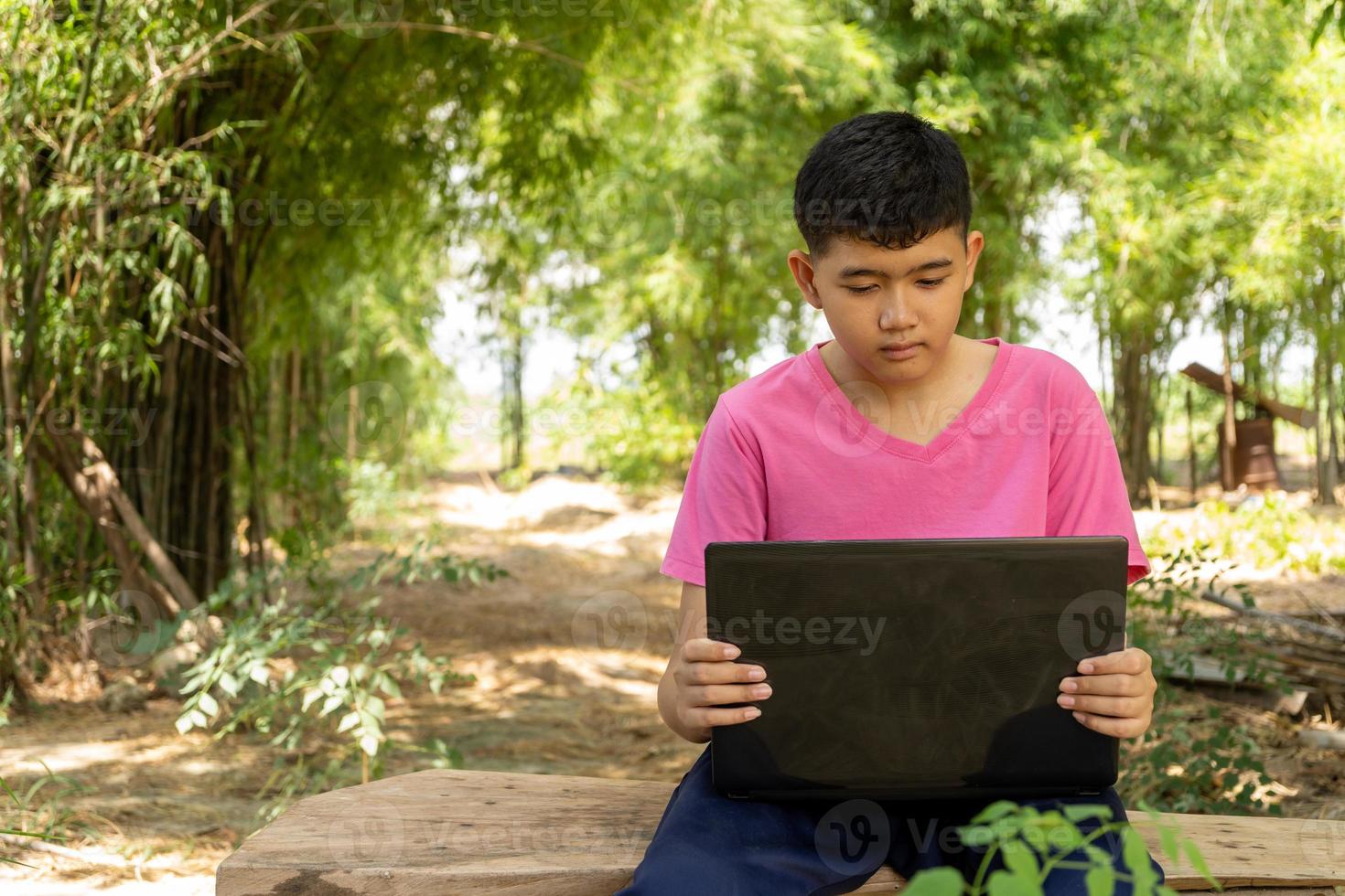 niño sentado en una silla estudiando en línea con una computadora portátil en casa en el campo foto