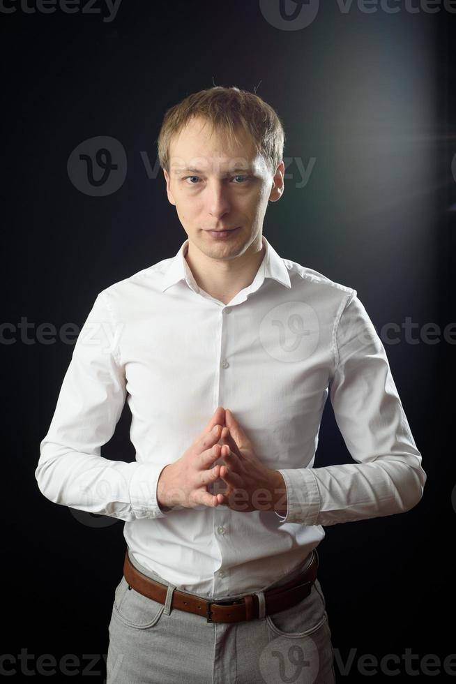 Cierra el retrato de un joven con camisa blanca y corbata negra, sonriendo mientras mira la cámara, contra el fondo del estudio. foto