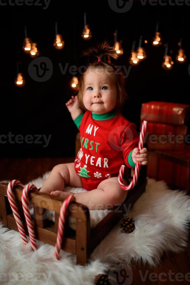 7 month old girl in a red Christmas costume on a background of retro garlands sits on a fur photo