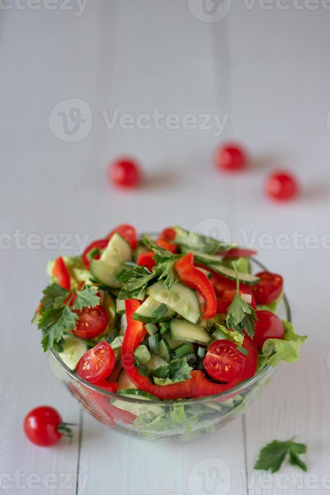 Salad on a white wooden background from tomatoes, cucumber, lettuce and red pepper. Healthy eating concept. photo